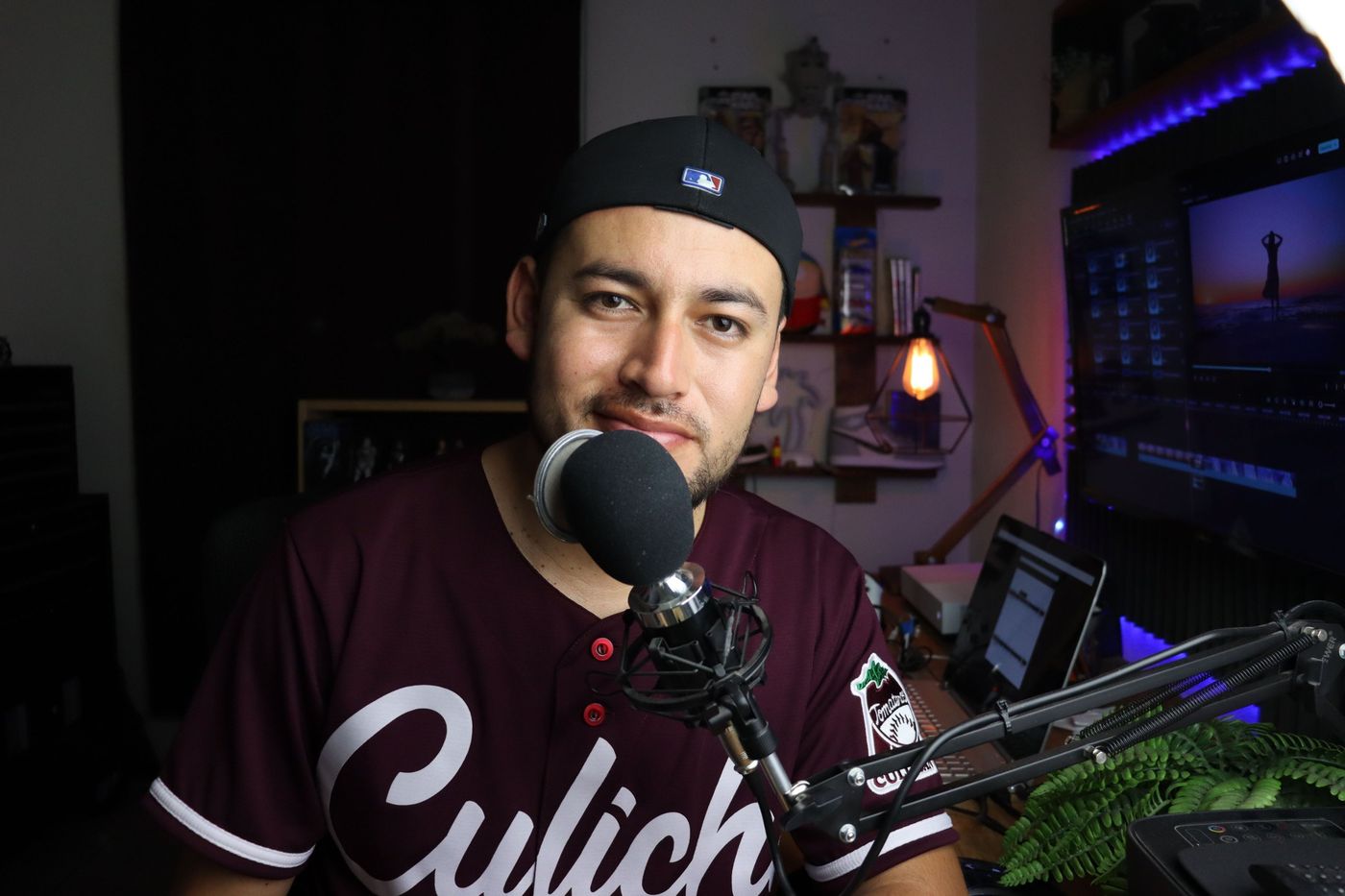 A broadcaster in a cap and jersey speaking into a boom-arm microphone