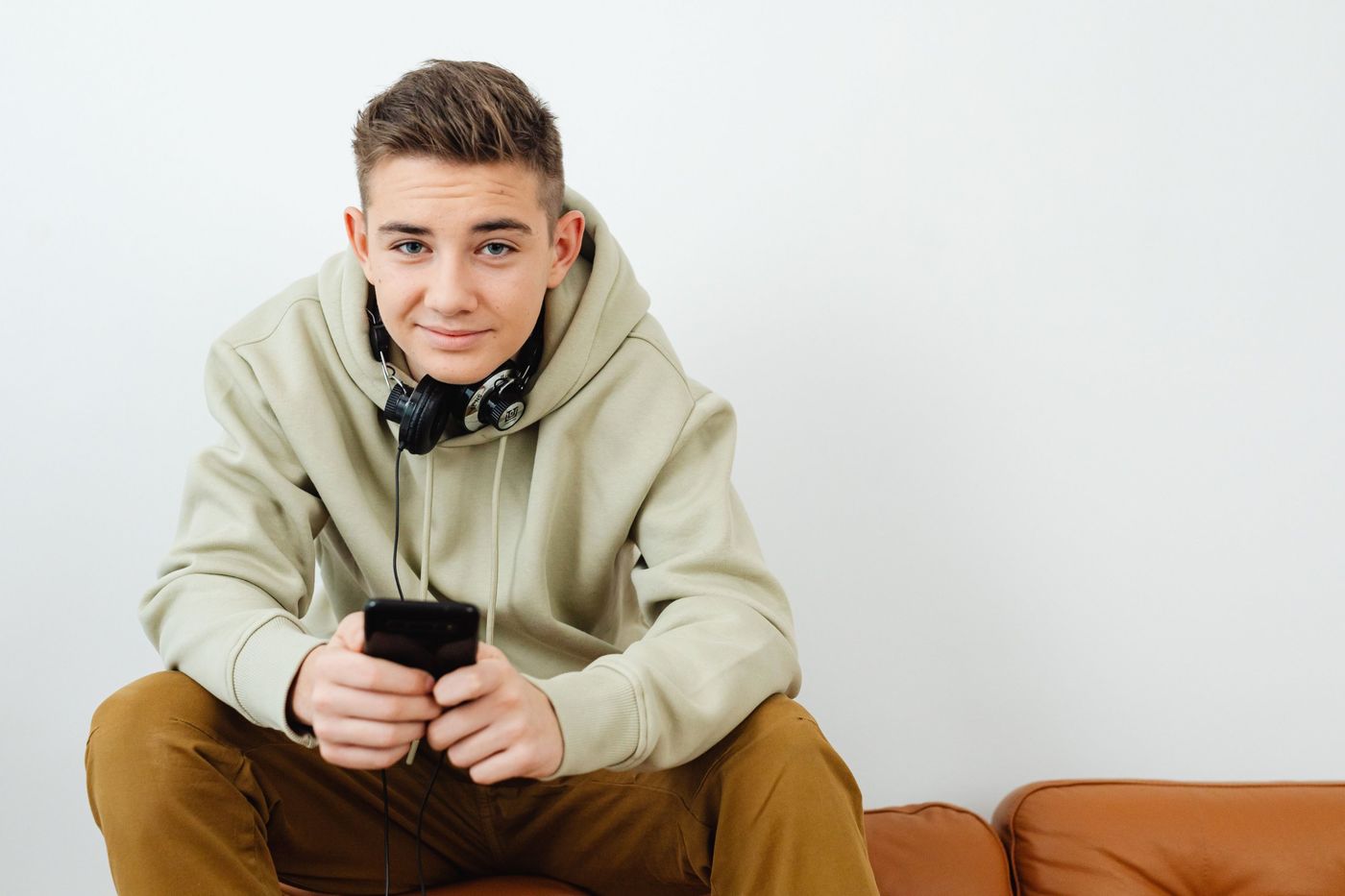 A young listener in a hoodie holding his phone on a sofa