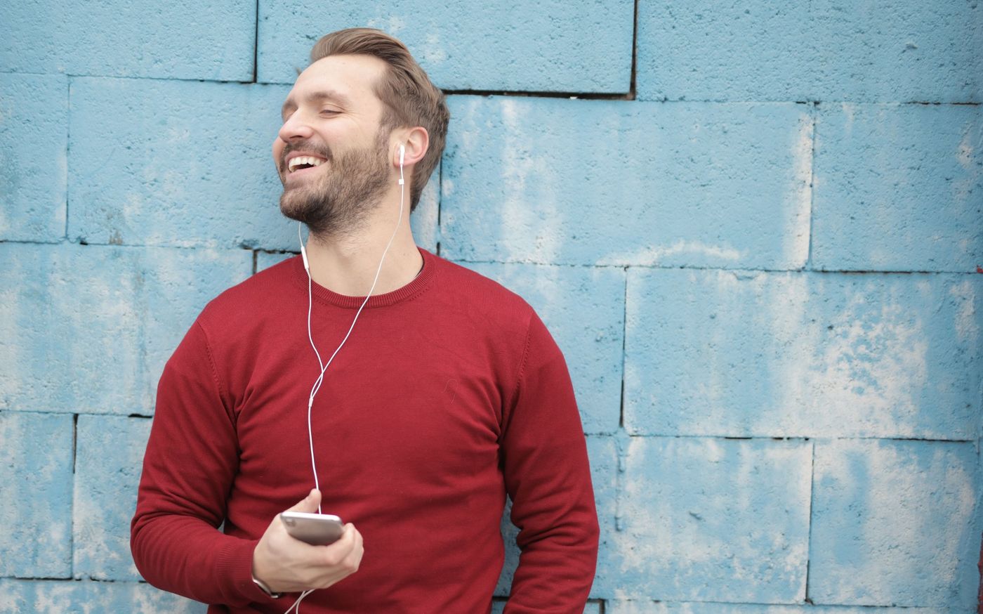 A man laughing as he listens on earphones with his phone