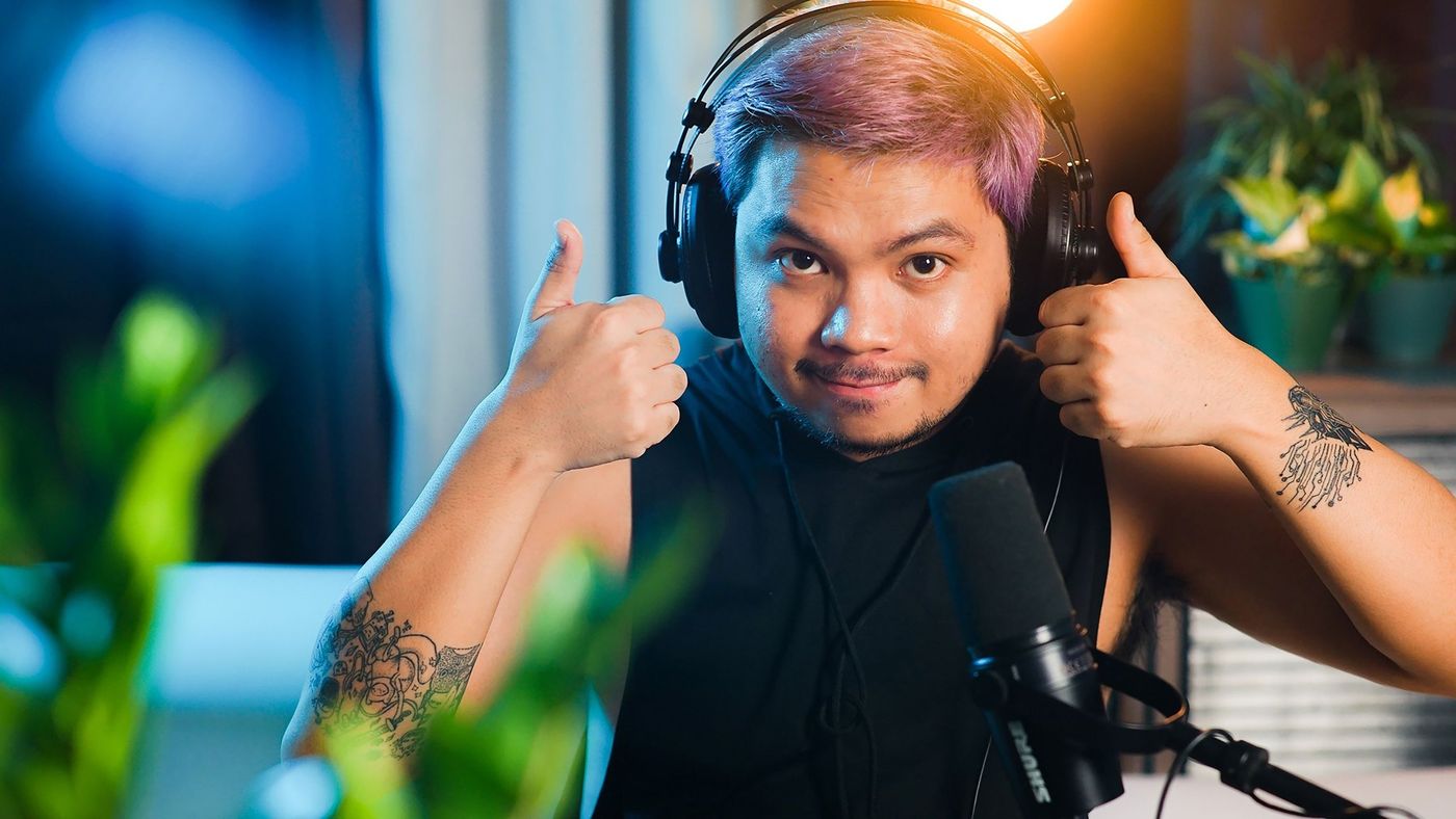 A presenter in headphones giving two thumbs up at his microphone